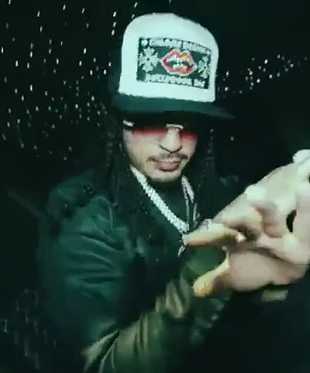 KMONEY in a white trucker cap and chain, hung in the gold frame of the back office